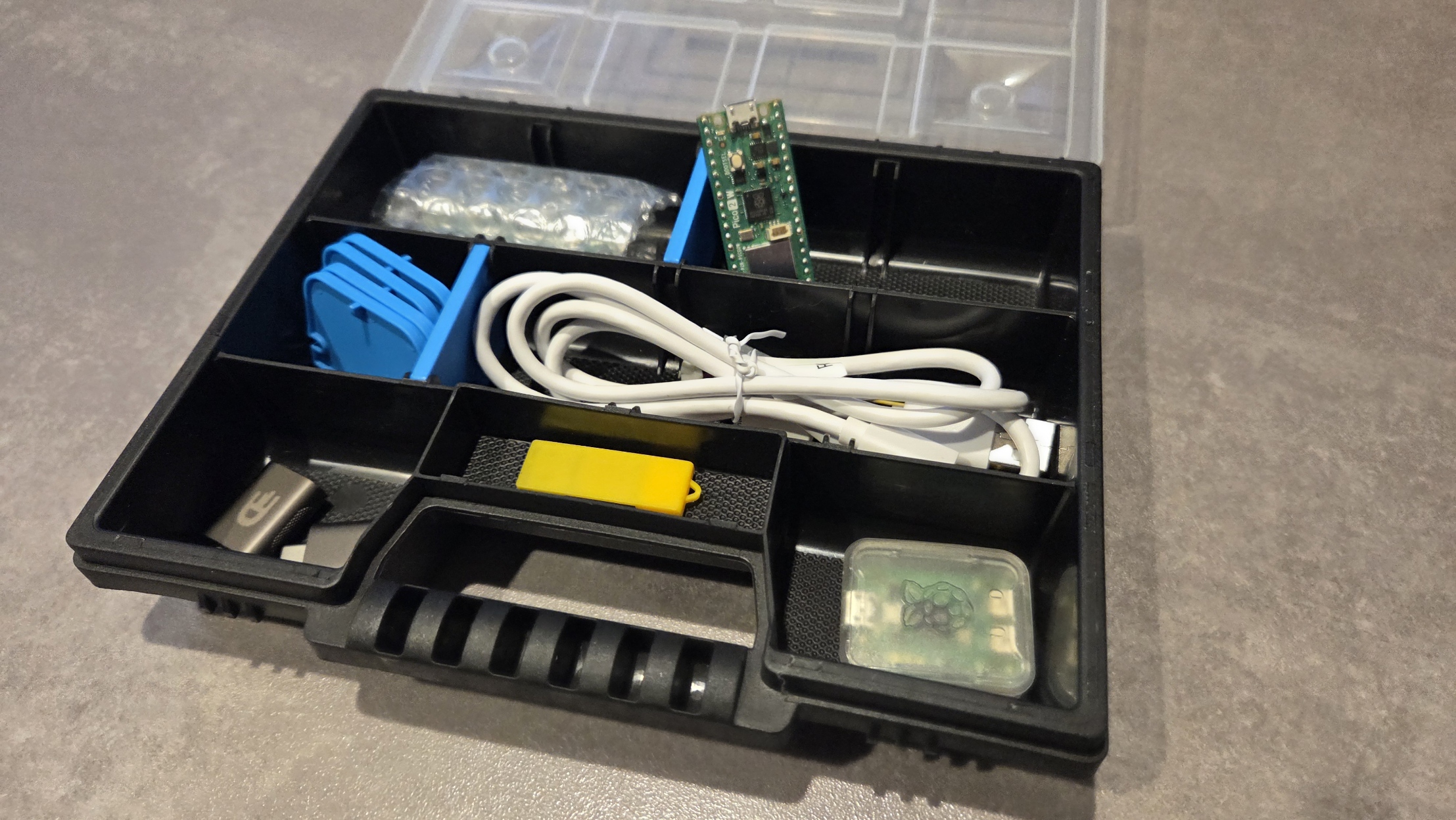 Assortment box opened, showing: Pico 2W boards, Debug probe, USB cable, USB-A to USB-C adapters, USB stick