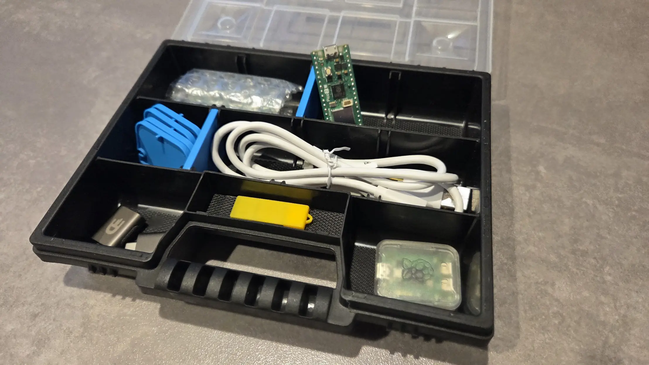 Assortment box opened, showing: Pico 2W boards, Debug probe, USB cable, USB-A to USB-C adapters, USB stick
